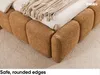 A close-up view of a bed with a textured boucle fabric base and a blanket draped over it, placed on a patterned rug. Produktbild-Vorschau