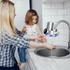 A woman and a child are in a kitchen, with the woman washing her hands under a faucet with a water filter attached. Produktbild-Vorschau