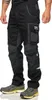 A person wearing black and gray Puma workwear pants and gray and yellow Puma sneakers, shown from the side against a white background. Produktbild-Vorschau