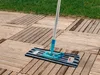 A mop with a blue and black striped cleaning pad rests on a wooden deck, with grass in the background. Produktbild-Vorschau