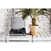 A vintage-style record player sits on a white wooden crate next to a potted palm plant, with a white brick wall in the background. Podgląd zdjęcia produktu
