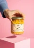 A hand holding a jar of lupines above a pink cube. Produktbild-Vorschau