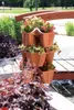 A tiered planter filled with flowers sits on a wooden deck next to a body of water. Náhľad obrázku produktu
