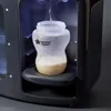 A close-up shot of a baby bottle being filled with water inside a Tommee Tippee Perfect Prep machine. Podgląd zdjęcia produktu