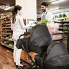 A woman is paying at a checkout counter in a store, with a double stroller in the foreground. Produktbild-Vorschau