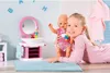 A young girl is lying on the floor, holding a baby doll next to a toy bathroom vanity with a sink and mirror. Podgląd zdjęcia produktu