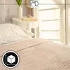 A close-up view of a beige blanket with a white pillow on a bed, with a side table and window in the background. Anteprima dell’immagine prodotto