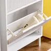 A white shoe cabinet with a tilted open drawer revealing two beige shoes inside. The background is split between white and yellow. Produktbild-Vorschau