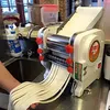 A person is using a commercial noodle maker in a kitchen or restaurant setting. Náhled obrázku produktu