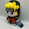 A plush toy of Naruto Uzumaki from Naruto Shippuden is displayed against a light gray and white background. The toy is standing upright and is accompanied by its packaging and a product tag. Anteprima dell’immagine prodotto