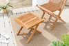 A wooden side table and chair on a patio rug, with a plant and flip-flops nearby. Produktbild-Vorschau