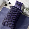 A bedroom scene with a bed made up with purple and black striped bedding, a matching pillow with a raven graphic, a floor lamp, and a rug. Produktbild-Vorschau