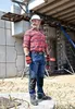 A construction worker wearing jeans and a red plaid shirt stands on a construction site. Produktbild-Vorschau