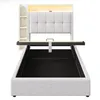 A bed frame with a headboard and storage compartments, shown from the front with the mattress support lifted. Produktbild-Vorschau