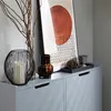 A close-up of decorative items and artwork on top of a gray cabinet. Náhľad obrázku produktu