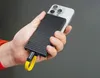 A hand holding a smartphone with a black carbon fiber patterned power bank attached to the back, connected by a yellow USB-C cable. Anteprima dell’immagine prodotto
