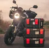 A motorcycle with three stacked toolboxes in front of it, parked on a dirt road during sunset. Anteprima dell’immagine prodotto