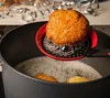 A piece of fried dough is being lifted out of a pot of hot oil with a slotted spoon. Produktbild-Vorschau