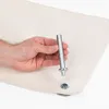 A hand is holding a metal tool over a piece of white fabric with an eyelet. Produktbild-Vorschau