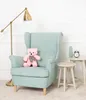 A pink teddy bear sits on a light blue armchair next to a small side table with a vase and an alarm clock. A floor lamp is to the left. Náhled obrázku produktu