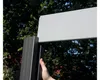 A hand is shown holding a dark gray fence post with a light gray fence panel above it, with trees in the background. Produktbild-Vorschau