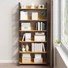 A tall, narrow bookshelf with multiple shelves filled with books and decorative items, placed against a light gray wall next to a window with sheer curtains. Produktbild-Vorschau