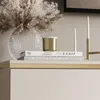 A close-up view of decorative items on a shelf, including a vase with dried flowers, a candle, and books. Produktbild-Vorschau