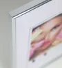Close-up of the corner of a silver picture frame with a white matting, showing a blurred image of a person's face with colorful makeup. Produktbild-Vorschau