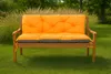 A wooden garden bench with orange and gray cushions sits on a green lawn, with tall grasses and trees in the background. Produktbild-Vorschau