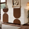 A modern white dresser with brown curved accents is shown in a well-lit room with a window and artwork on the wall. Voir les images du produit