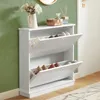 A white shoe cabinet with two flip-down drawers, filled with shoes, is shown in a room with a green wall and a wooden floor. Produktbild-Vorschau