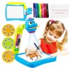 A young girl is using a drawing projector to trace a horse onto a piece of paper. The projector is a toy with a blue cartoon character head and a light beam. There are also marker pens and projection discs shown. Náhled obrázku produktu