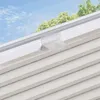 A close-up view of a pleated blind attached to a window frame, with trees and sky visible in the background. Produktbild-Vorschau