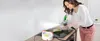 A woman is cleaning a stovetop with a steam cleaner in a kitchen. Náhled obrázku produktu