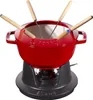 A red Staub fondue set with wooden-handled fondue forks is displayed on a black stand. Voir les images du produit