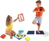 Two children are playing a yoga game. The boy is in a tree pose, and the girl is holding up a card with a reindeer doing a yoga pose. Produktbild-Vorschau