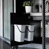 Two white bins with black handles are shown inside a black cabinet. A small green plant in a white pot sits on a shelf above the bins. Produktbild-Vorschau