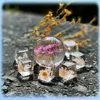 Several clear resin cubes and a sphere containing dried flowers are arranged on a dark, textured surface, with dried yellow flowers in the background. Voir les images du produit