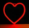 A red neon heart-shaped lamp is mounted on a black background and rests on a wooden surface. Voir les images du produit