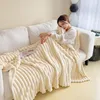 A woman is sleeping on a couch, covered by a thick, cream-colored blanket. Produktbild-Vorschau