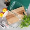 Two glass baking dishes are placed on wooden cutting boards, with apples, a bottle of oil, and spice grinders in the background. Produktbild-Vorschau