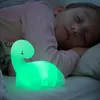 A child sleeping next to a glowing dinosaur night light. Voir les images du produit