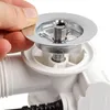 A close-up shot of a person's hand holding a metal drain cover over a white plastic plumbing fixture. Produktbild-Vorschau