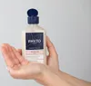 A hand holding a bottle of Phyto Repair Repairing Shampoo. Podgląd zdjęcia produktu