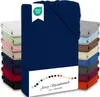 A stack of folded fitted sheets in various colors, with a navy blue fitted sheet prominently displayed in the foreground. A white label with a green OEKO-TEX logo is attached to the navy blue sheet. Produktbild-Vorschau