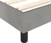 A close-up view of the corner of a grey upholstered bed frame with wooden slats visible inside. Voir les images du produit