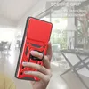 A hand holding a red phone case with a ring holder, with a blurred indoor background. Produktbild-Vorschau