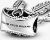 A close-up view of a silver charm with feather details and the inscription "FOLLOW YOUR DREAMS". Produktbild-Vorschau