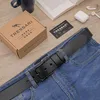 A black leather belt is laid across blue jeans, with a Tressari branded box and card nearby, along with a book and wireless earbuds. Produktbild-Vorschau