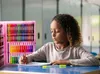 A young girl is drawing at a table with a large art supply case open next to her. Podgląd zdjęcia produktu